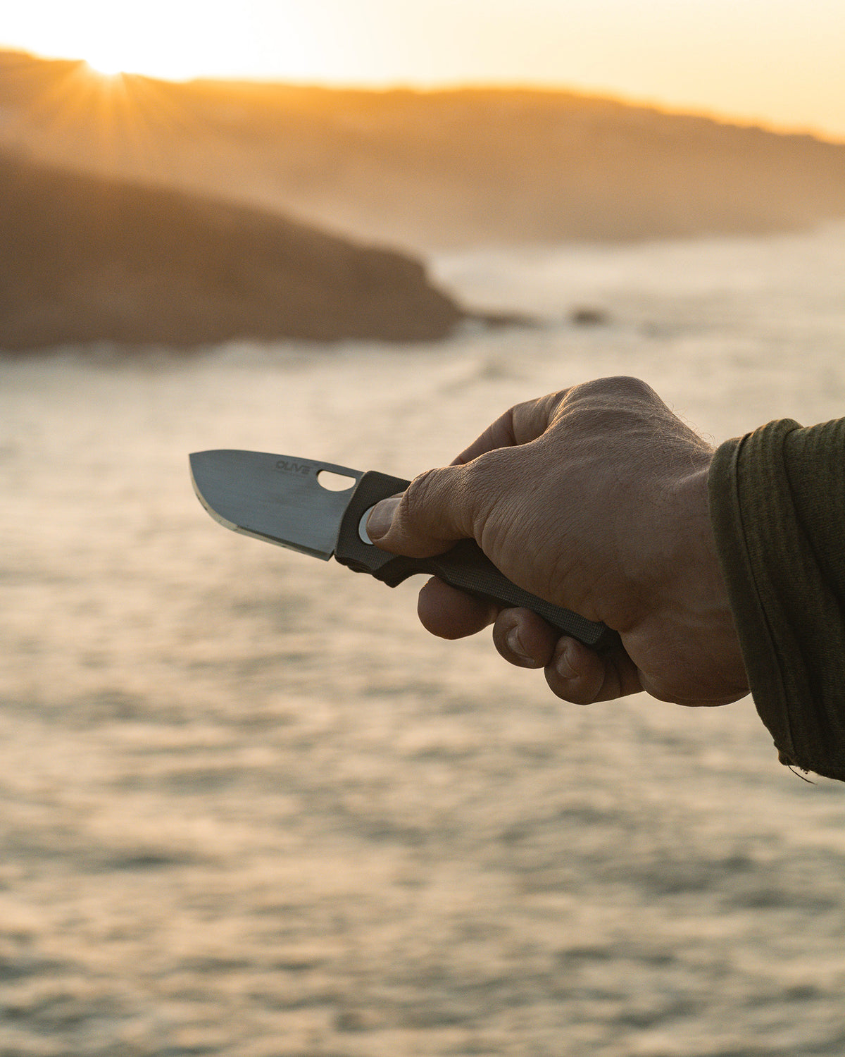 Olive Knives LENTA EDC folding knife, Elmax steel — lifestyle, held at the coast during sunset