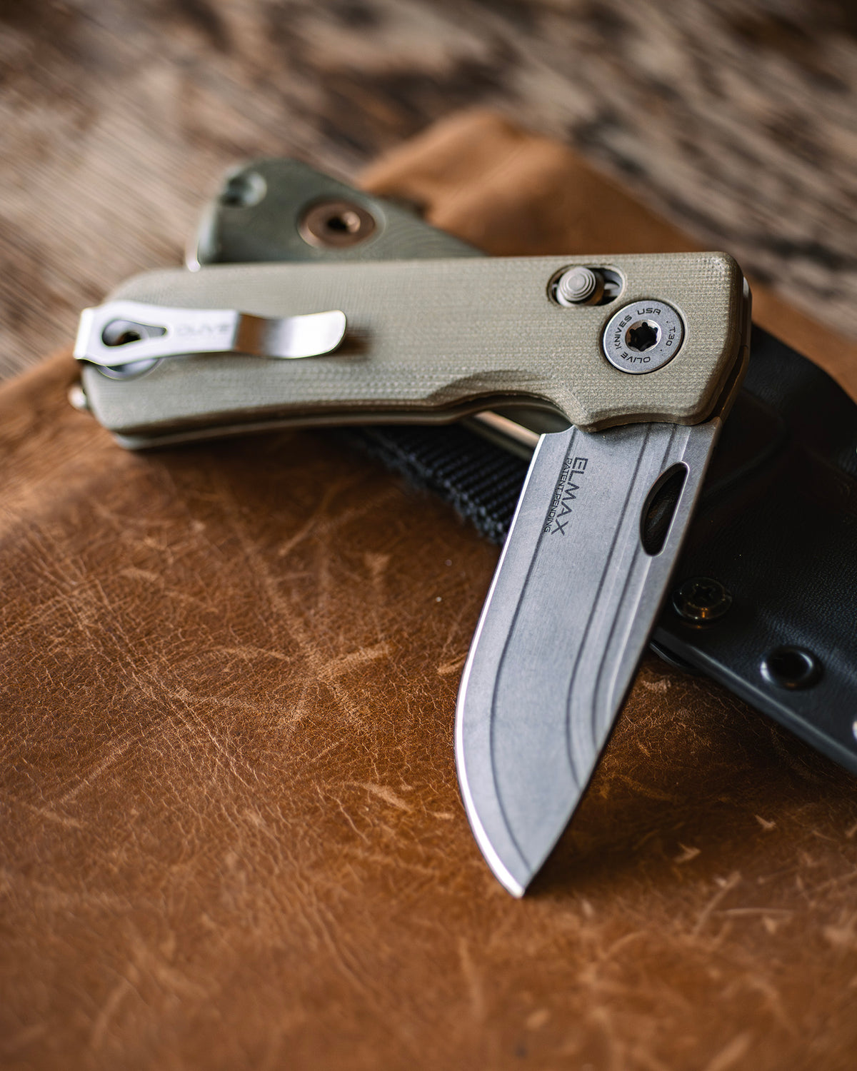 Olive Knives LENTA EDC folding knife, Elmax steel — lifestyle, beside a leather journal and its sheath