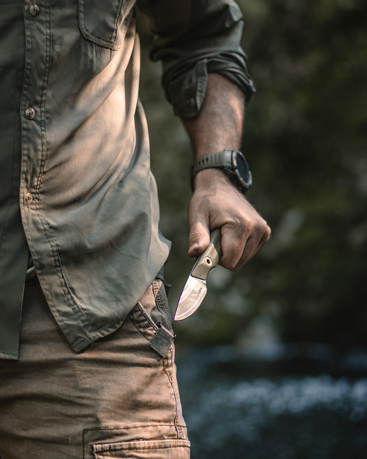Olive Knives VENARI compact EDC fixed blade knife, Elmax steel — lifestyle, pulled from a pocket beside a creek