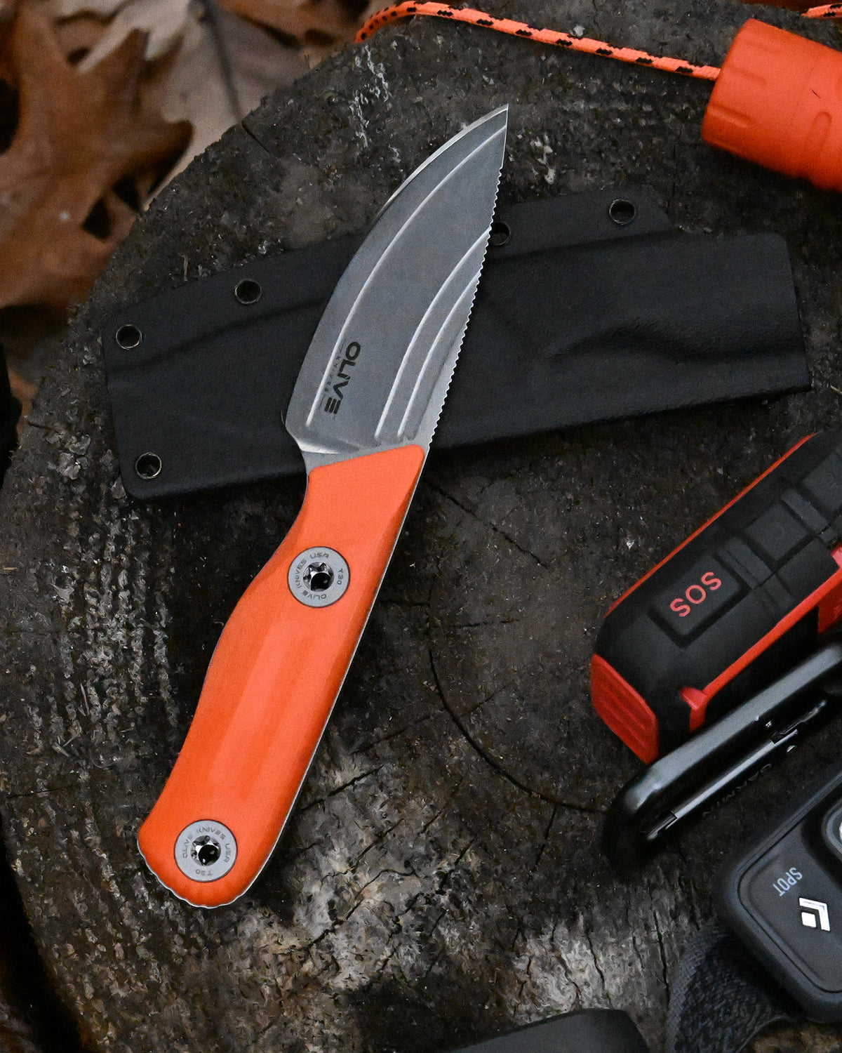 Olive Knives VENARI compact EDC fixed blade knife, Elmax steel — lifestyle, on a tree stump beside an emergency SOS device